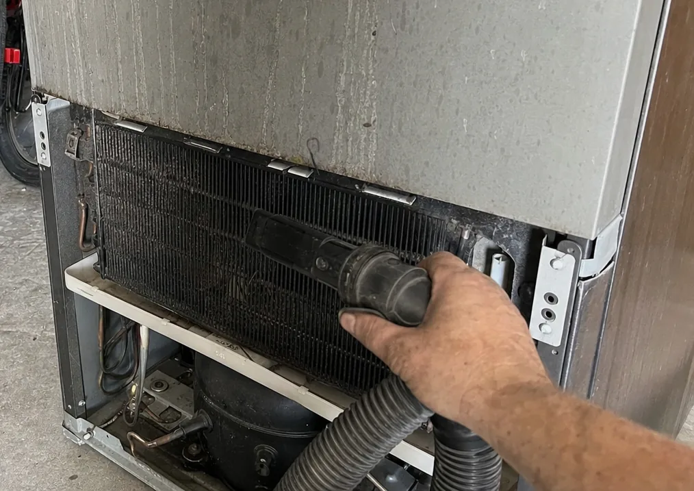 The compressor and its suction line sitting under a condenser coil, reached through the removed lower grille.