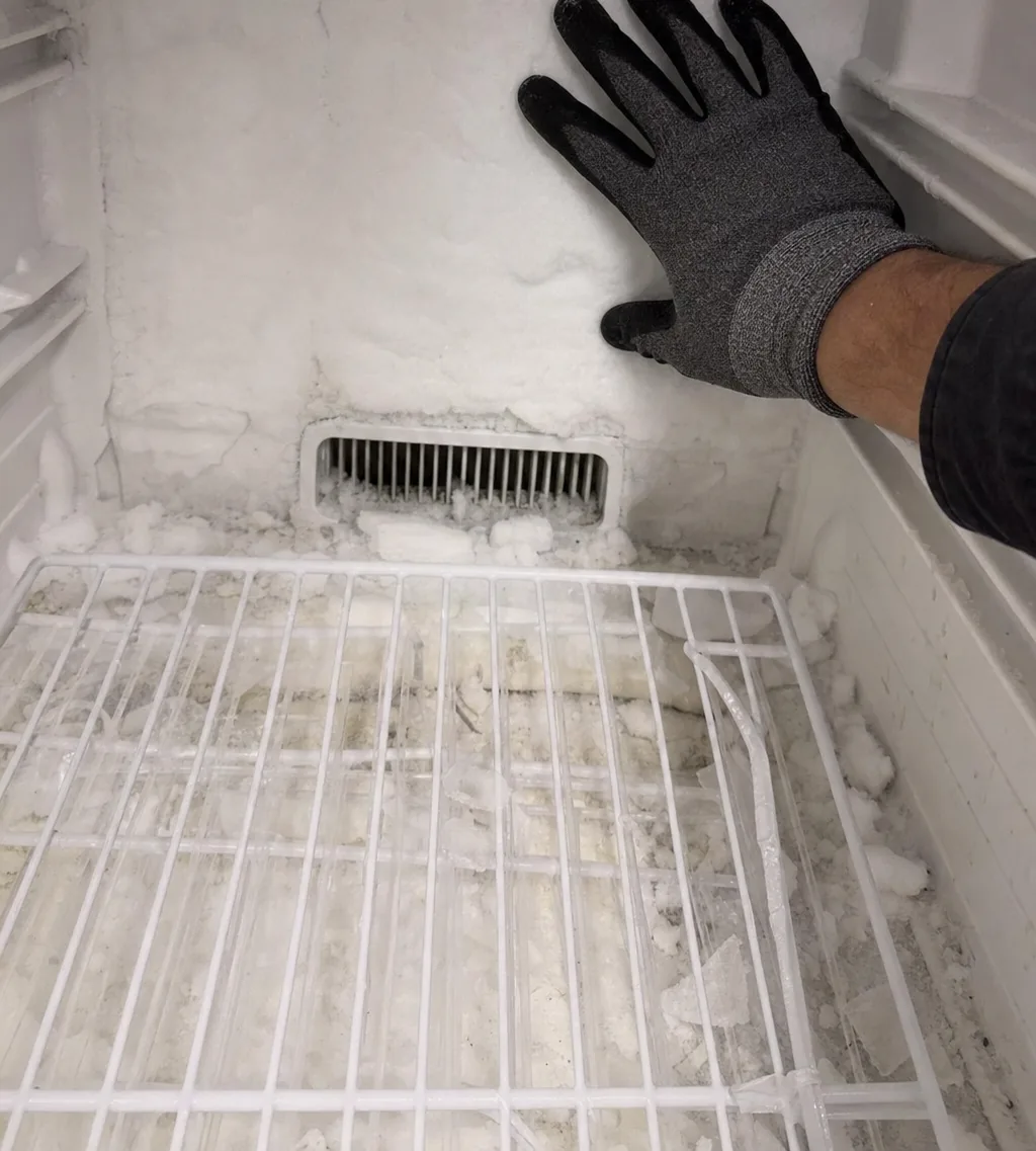 The return-air vent at the foot of a freezer back wall, half-blocked by built-up frost.