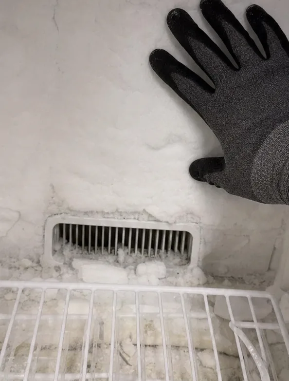 Loose ice and broken frost sitting on a wire freezer shelf beneath a frosted return-air vent.