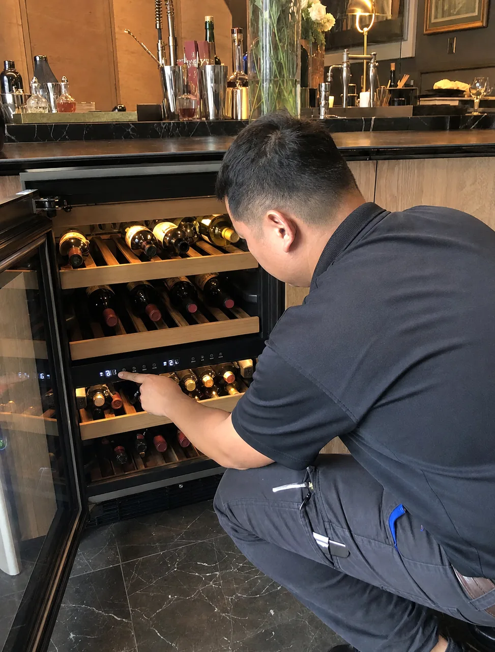 A built-in wine cabinet in a dark-tiled bar area, its door held open while the temperature is set.